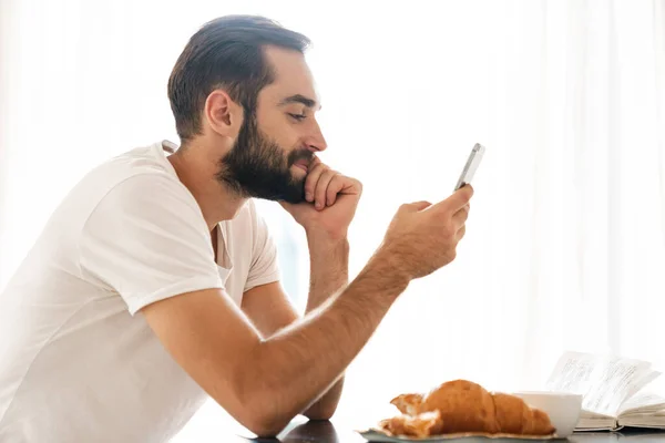 Man indoors at home have a breakfast using mobile phone. — 图库照片