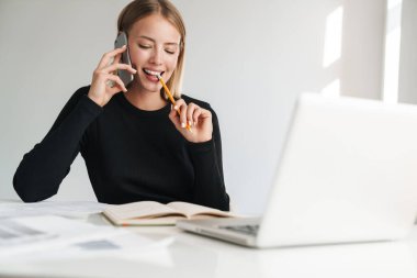 Smiling young blonde business woman talking by phone.