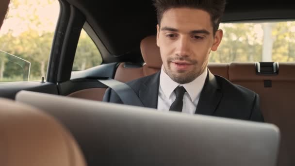 Arabada Otururken Dizüstü Bilgisayar Kullanan Konsantre Olmuş Yakışıklı Adamı — Stok video