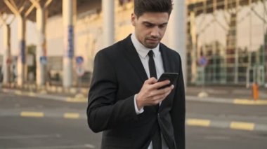 Ciddi yakışıklı işadamı havaalanının yakınındaki park yerinde yürürken akıllı telefon kullanıyor.