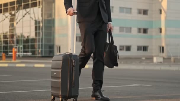 荷物を持って歩いて空港の近くの駐車場を離れて見て クールな自信を持ってハンサムなビジネスマン — ストック動画