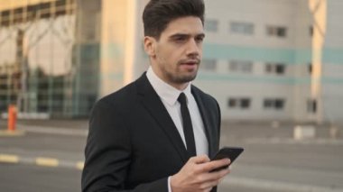 Havaalanının yakınındaki otoparkta yürürken akıllı telefon kullanan ciddi yakışıklı işadamının görüntüsünü kapat.