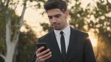 Kendine güvenen yakışıklı iş adamı dışarıda akıllı telefon kullanıyor.