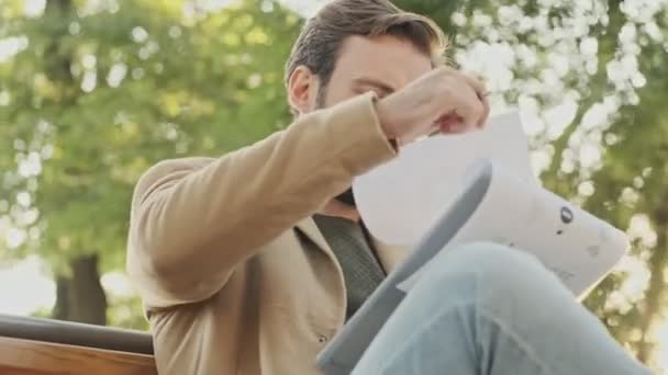 Mosolygó Elegáns Szakállas Férfi Kabátban Újságot Olvas Miközben Parkban Üldögél — Stock videók