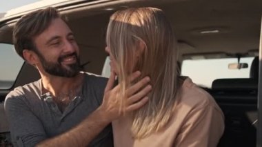 Güzel genç bir çift arabanın bagajında otururken birbirlerine bakıyorlar.