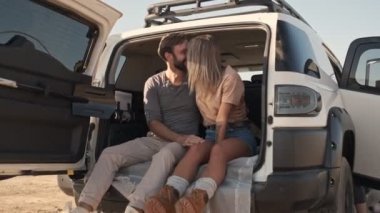 Genç ve neşeli bir çift arabanın bagajında eğlenirken gülümsüyor.