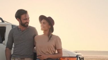 Sevimli genç bir çift yazın gölün kenarında SUV arabasının yanında dururken sarılıyorlar.