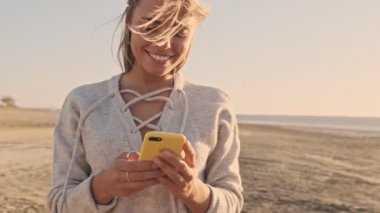 Güzel, gülümseyen bir kadın gölde yürürken akıllı telefon kullanıyor.