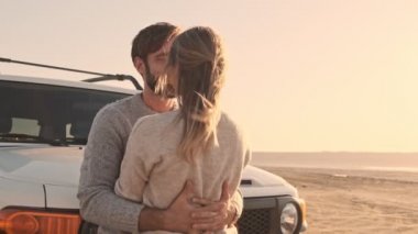 Genç bir çift yazın gölün kenarında SUV arabasının yanında öpüşüyorlar.