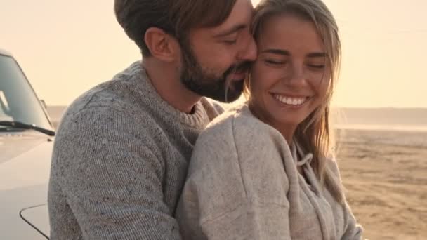 一对恋爱中的年轻夫妇站在湖边的越野车旁拥抱亲吻着 — 图库视频影像
