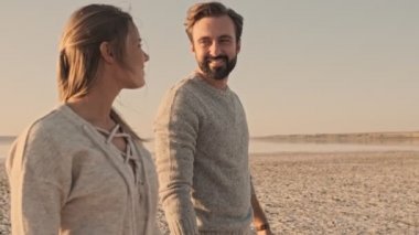 Güzel bir çift, yazın göl kenarında el ele yürürken birbirlerine bakıyorlar.