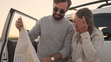 Genç bir çift göl kenarında arabanın yanında dururken haritaya bakıyorlar.