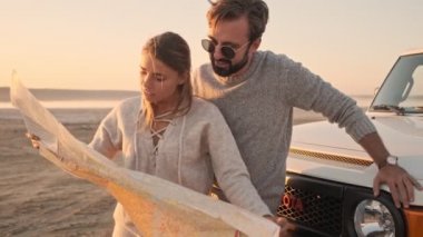 Olumlu genç bir çift göl kenarındaki arazi aracının yanında haritayı tutarken bölgeyi keşfediyorlar.