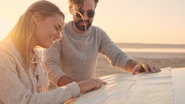 一对积极的年轻夫妇一边说着话 一边发现了地图 并把它放在海滩上的车篷上 — 图库视频影像