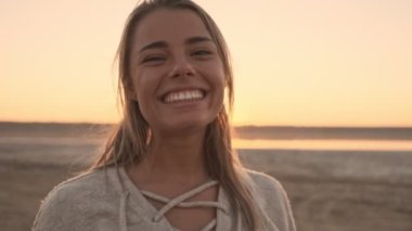 Çekici, mutlu bir genç kadın, şafak vakti gölün yanında dururken kameraya gülümsüyor.