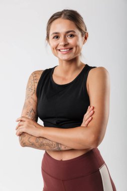 Spor kıyafetli, gülümseyen ve kollarını kavuşturmuş beyaz arka planda izole bir kadın resmi.