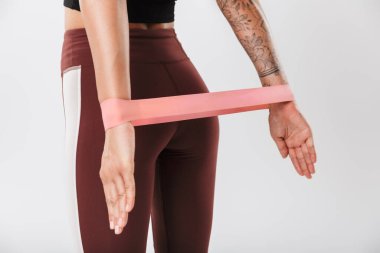 Spor kıyafetli genç bir kadının beyaz arka planda izole edilmiş daha geniş ekipmanlarla spor yaparken görüntüsü.