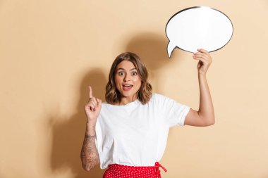 Kırmızı etekli şaşırmış bir kadın bej arka planda boş düşünce balonunu tutarken işaret ediyor.