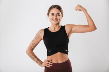 Çekici, gülümseyen, formda, beyaz arka planda duran, kaslarını esneten genç bir sporcu kız.