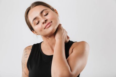 Spor kıyafetli esmer bir kadının beyaz arka planda antreman yaparken boynuna dokunuşu.