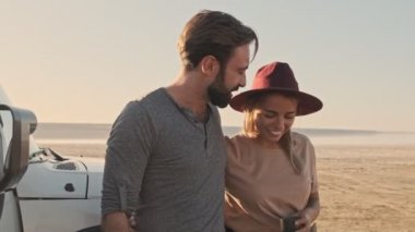 Mutlu ve genç bir çift yazın gölde arazi aracının yanında dururken çay ya da kahve içiyorlar.