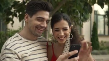 Sevimli bir çift akıllı telefondan komik bir şey izliyorlar. Şehir caddesinde bankta otururken.