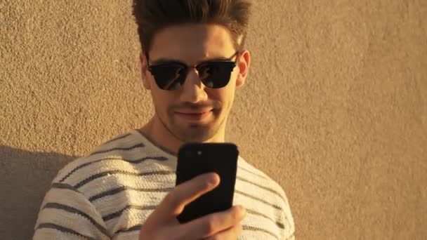 Ένας Όμορφος Άντρας Καθημερινά Ρούχα Και Γυαλιά Ηλίου Χρησιμοποιεί Smartphone — Αρχείο Βίντεο