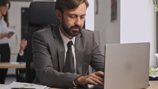 オフィスのテーブルに座っている間 ラップトップコンピュータを使用して その後リラックスして正式な訴訟で深刻なビジネスマン — ストック動画
