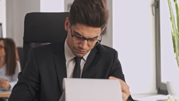 オフィスのテーブルに座っている間にクリップボードと文書を勉強正式な訴訟や眼鏡の深刻なビジネスマン — ストック動画