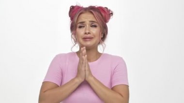 Renkli, pembe saçlı güzel bir kadın ellerini birarada tutarken beyaz arka planda dua ediyor.