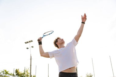 Spor kıyafetli yakışıklı bir adamın dışarıda tenis oynarken raket tutuşu.