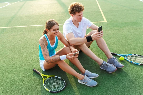 Приваблива Пара Здорових Тенісистів Використовує Мобільні Телефони Сидячи Галявині Стадіоні — стокове фото