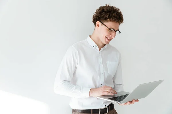 年轻英俊 满脸笑容的卷发商人 身穿白衬衫 站在与世隔绝的背景下 在笔记本电脑上工作 — 图库照片