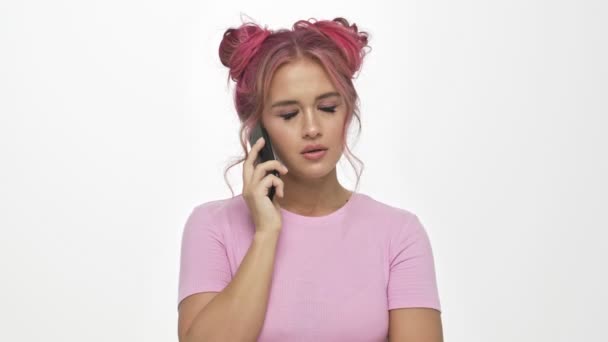 一位有着粉色发型的不高兴的年轻女子一边打电话一边用白色背景来掩饰自己的不满 — 图库视频影像
