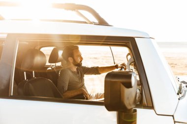 Yakışıklı, ciddi bir delikanlının plajda arabayı sürüşünün görüntüsü..