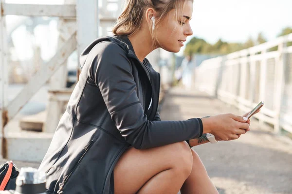 Hermosa Joven Deportista Sentada Puente Escuchando Música Con Auriculares Sosteniendo — Foto de Stock