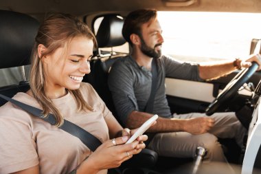 Sahilde, arabada sevişen genç, pozitif çiftin görüntüsü. Cep telefonu kullanan kadın.