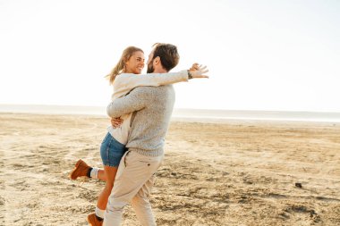 Güzel genç bir çift güneşli sahilde dikiliyor, sarılıyorlar.