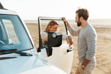 Genç, mutlu, sevgi dolu bir çiftin fotoğrafı plajda, arabanın yanında..