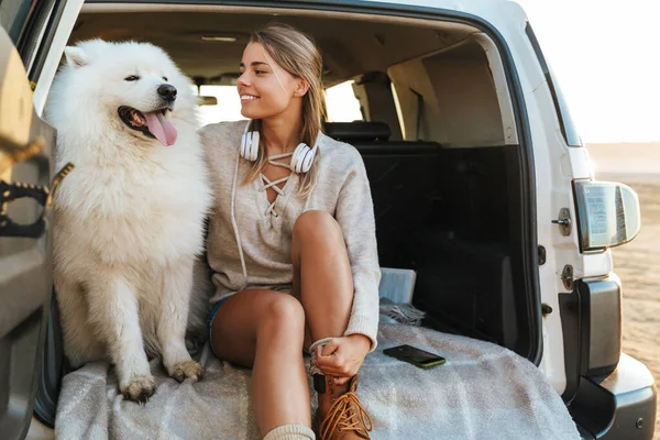 Obraz Pozytywnej Młodej Kobiety Przytulającej Psa Samoyed Zewnątrz Plaży Samochodzie — Zdjęcie stockowe