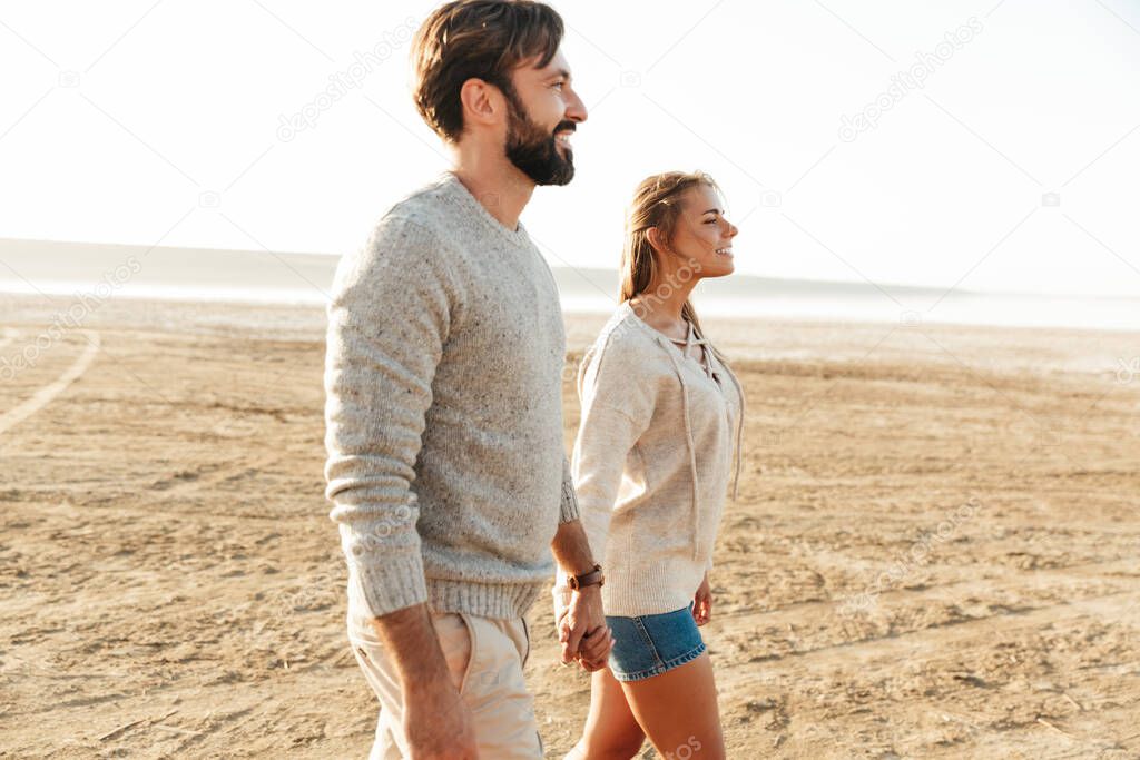 Photo of young positive loving couple outdoors at beach walking.