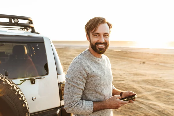 Glimlachende Jongeman Met Behulp Van Mobiele Telefoon Terwijl Hij Bij — Stockfoto