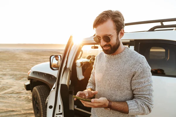 Glimlachende Jongeman Met Behulp Van Mobiele Telefoon Terwijl Hij Bij — Stockfoto