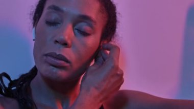 Kulaklıklı, memnun Afrikalı spor kadını, müzik dinlerken ve o anın tadını çıkarırken, duvarın yanında izole edilmiş el fenerlerinin arka planında otururken.