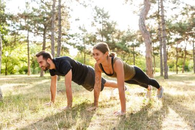 Genç, mutlu, neşeli bir spor kadını ve erkeğin doğa yeşil parkında şınav çekerken görüntüsü..