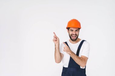 Kasklı neşeli genç bir inşaatçının beyaz duvar arkasına izole edilmiş pozu..
