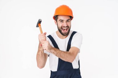 Kasklı, beyaz duvar arkasında çekiç tutan mutlu bir genç adam görüntüsü..