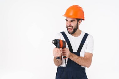 Çığlık atan, kasklı, duygusal genç bir adamın fotoğrafı. Arka planda, elinde matkap olan beyaz duvar arkasında izole edilmiş..