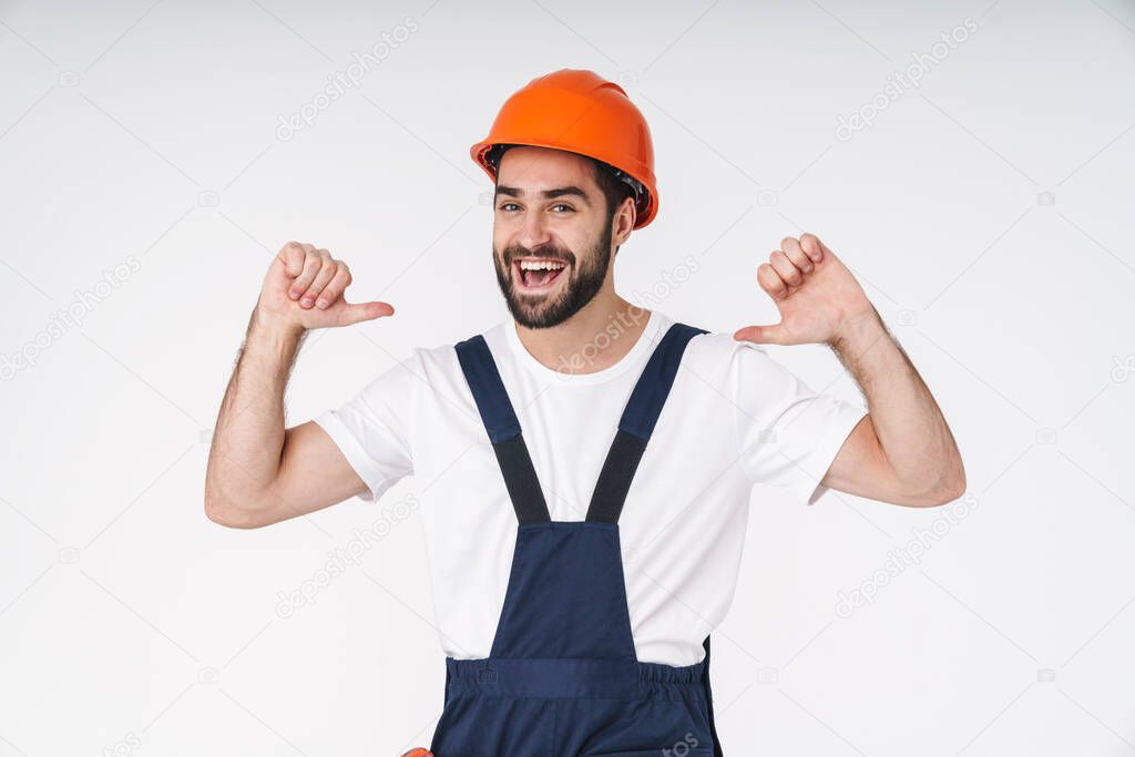 Photo of a cheery optimistic young man builder in helmet posing isolated over white wall background pointing to himself.
