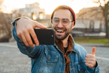 Yakışıklı, mutlu, genç, şık sakallı bir adamın sokakta yürürken selfie çekmesini.